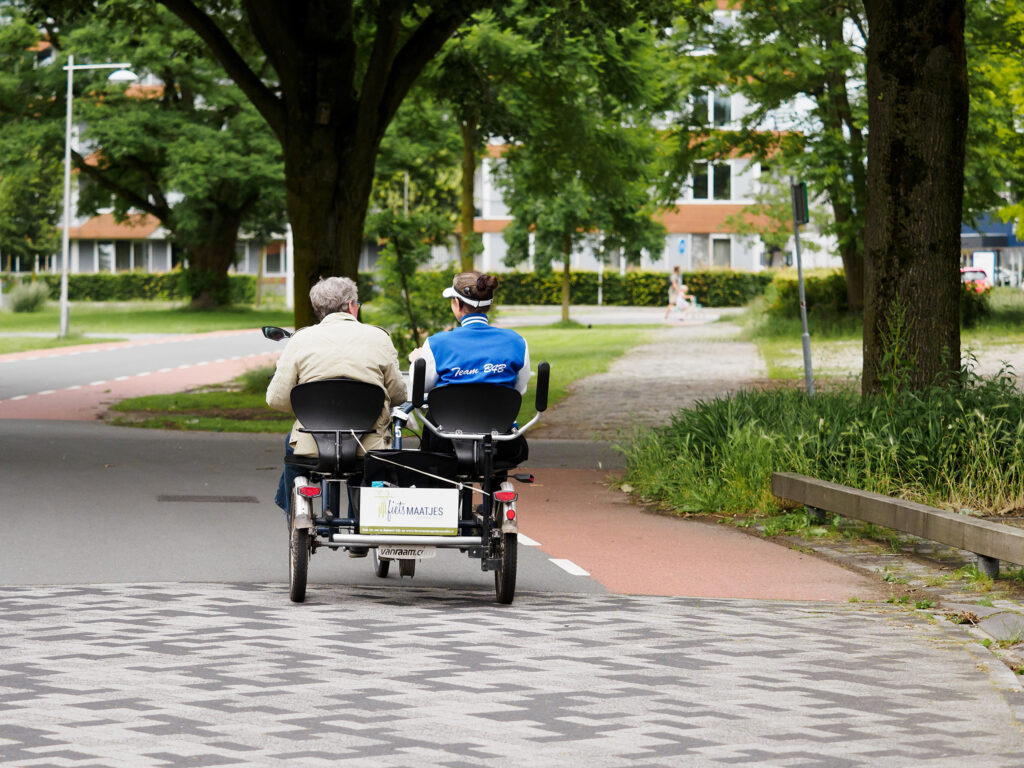 Op de afbeelding een deelnemer en de chauffeur van de duofiets die samen over de weg fietsen.