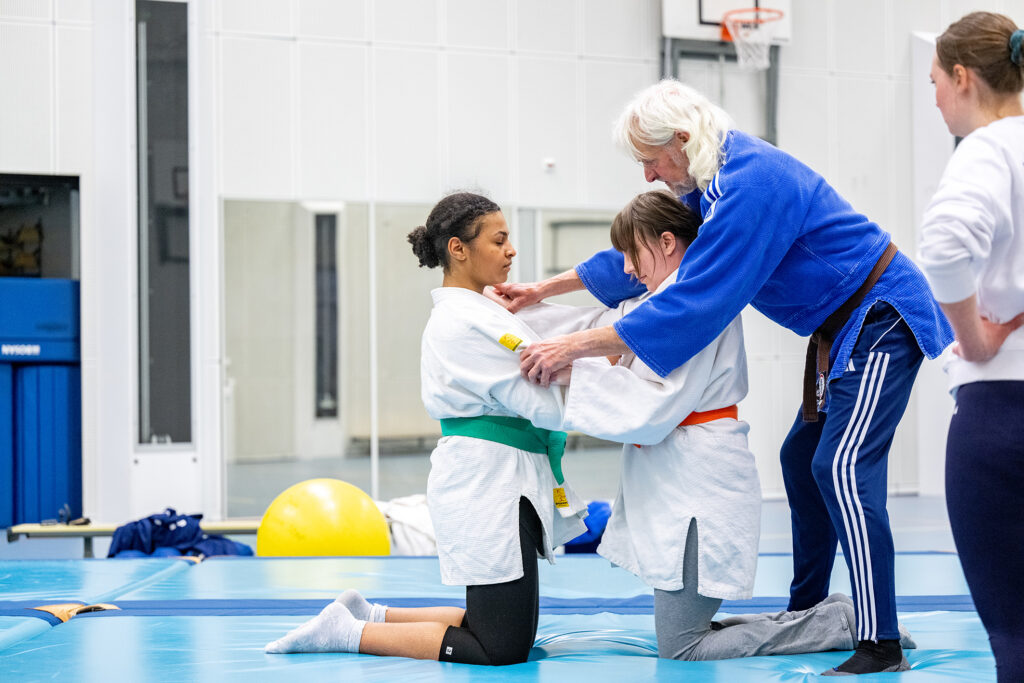 Judo-instructeur instrueert twee deelnemers hoe ze elkaar moeten vastgrijpen.