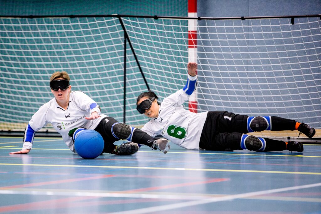 twee goalballers duiken naar de bal om hun doel te verdedigen