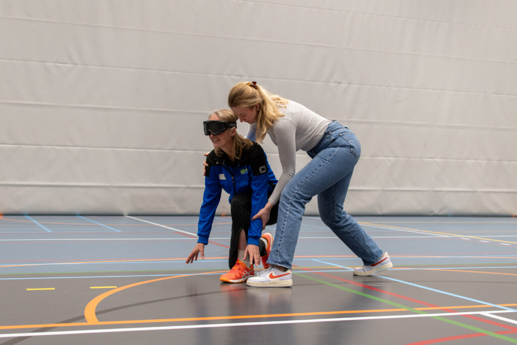 sporter met geblindeerde bril wordt begeleid door een coach
