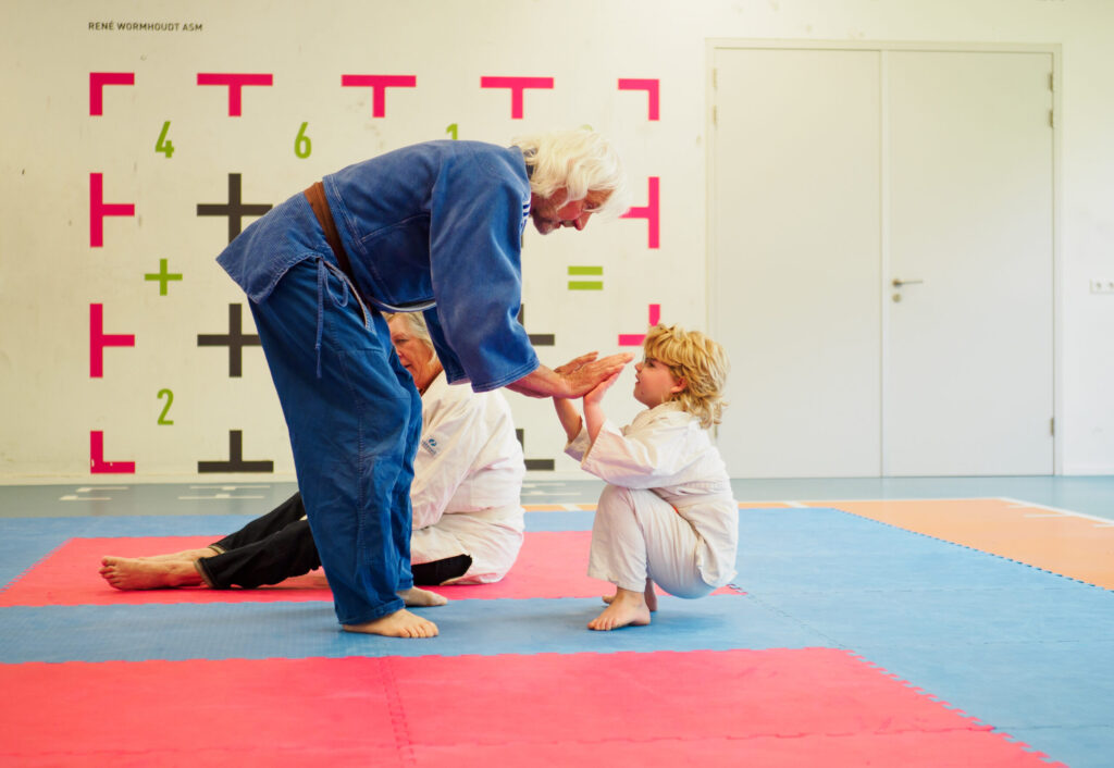 een jongere en oudere judoka samen op de mat