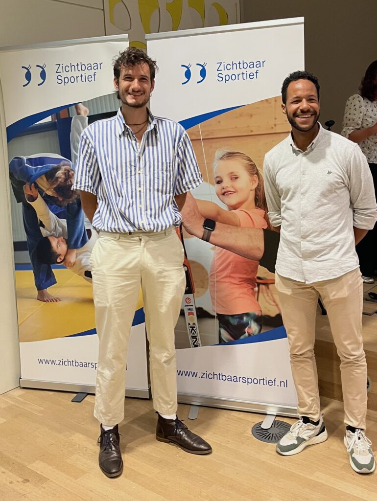 melvin en chris vrolijk poserend bij de banners van zichtbaar sportief