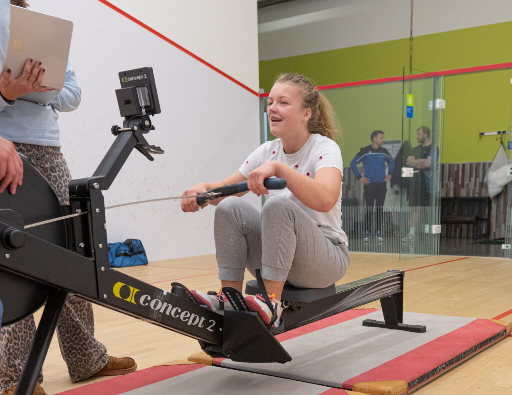 Deelnemer multisportdag op een ergometer aan het roeien.