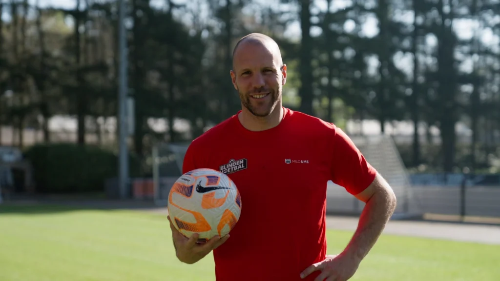 Portretfoto Ron Vlaar blindenvoetbal VIPS met een bal in zijn hand staand op een voetbalveld.