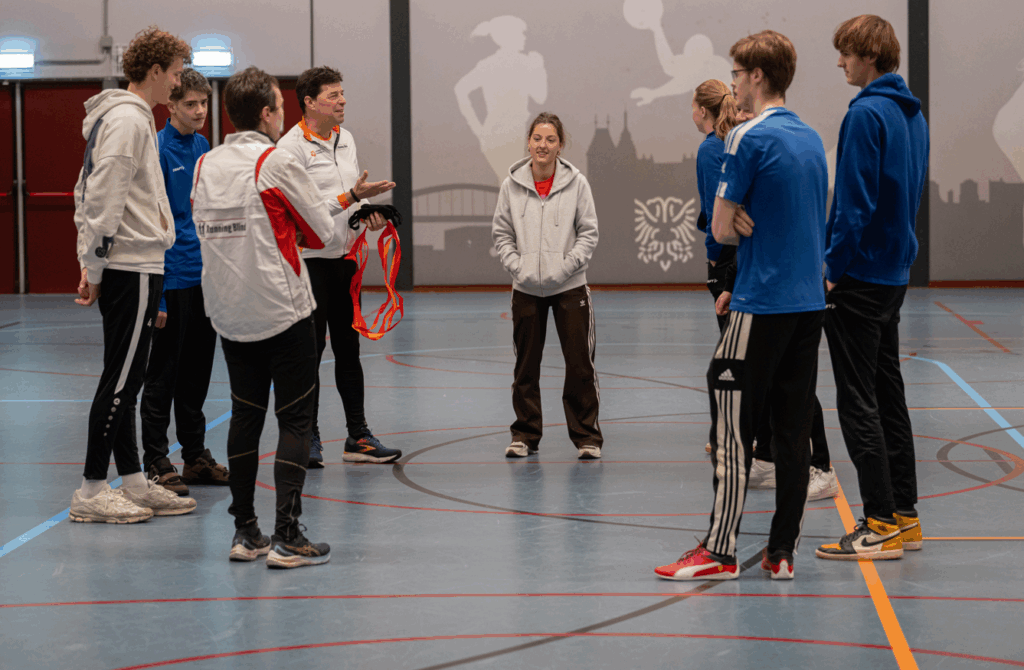 instructeur geeft uitleg aan een zestal deelnemers aan de running blind clinic in de sportzaal